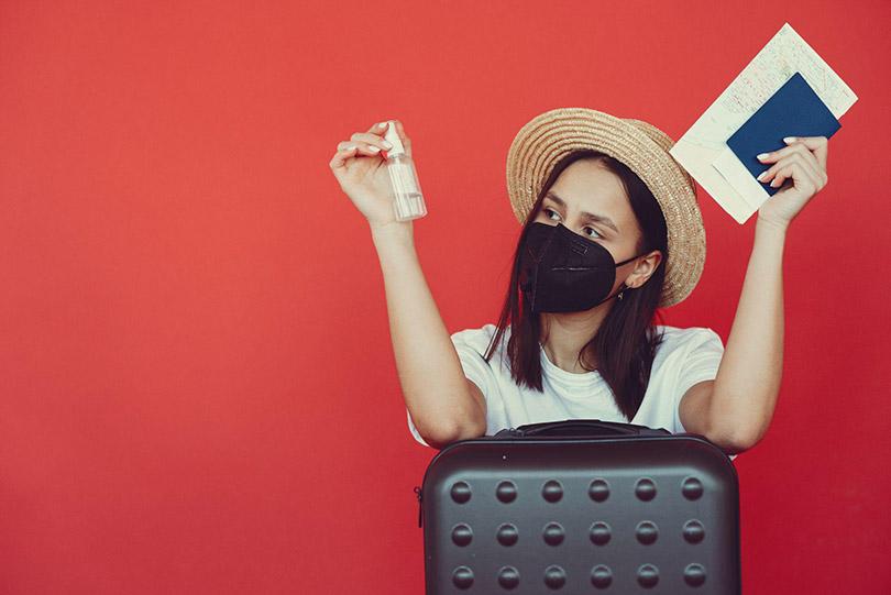 Mulher protegida contra a Covid-19 com mala e passaporte.