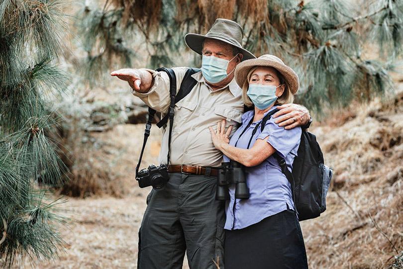 Casal viajando na natureza usando máscara.