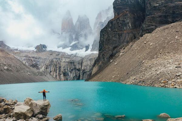 Homem de braços abertos em lago da Patagônia