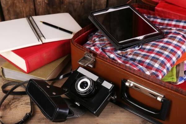 Mala de viagem com câmera, roupas, tablet e livros.