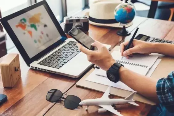 homem pesquisando sobre viagens com computador, celular, globo e outros itens relacionadas a viagens por perto