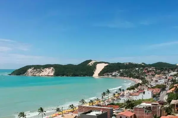 Praia de Ponta Negra, em Natal. Mar e céu azuis, areia e casas.