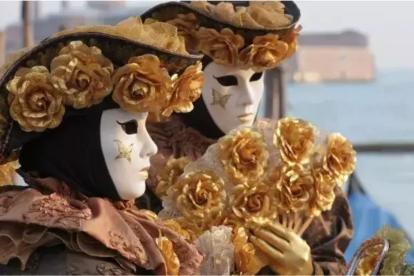 Casal com vestes tradicionais do carnaval de Veneza, com máscaras e roupas de época na cor dourada