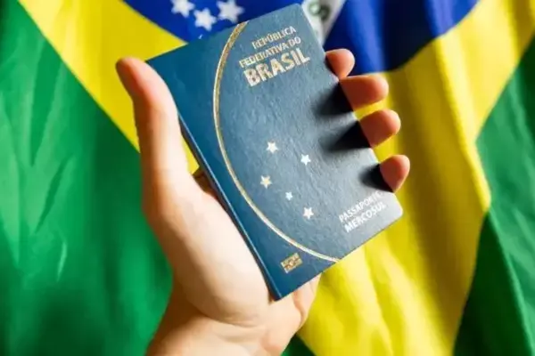 Pessoa segurando passaporte brasileiro em frente a uma bandeira do Brasil