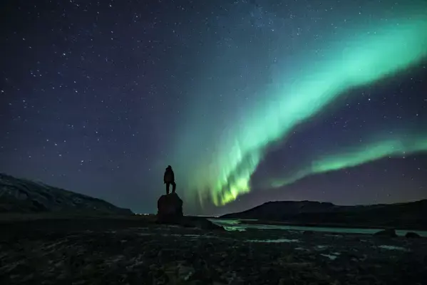 Homem em pé em cima de carro observando a aurora boreal