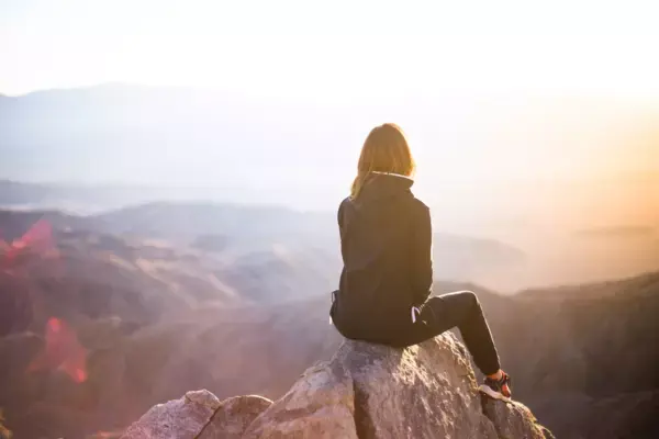 Mulher observando paisagem sentada em uma rocha