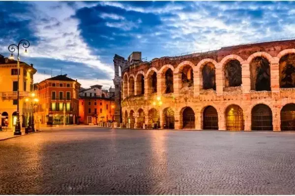 Visão de rua de Verona ao entardecer, com prédios antigos ao fundo e parte da arena