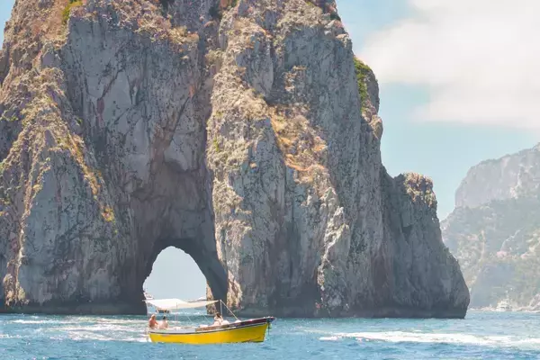 Um pequeno barco amarelo em frente aos Faraglioni, na Ilha de Capri, Itália.