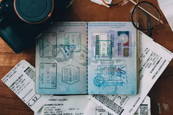 Imagem de um passaporte aberto em cima de passagens de voo e alguns objetos em volta.