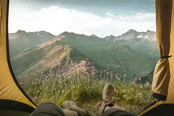 Foto de pessoa deitada dentro de uma barraca admirando a paisagem montanhosa.