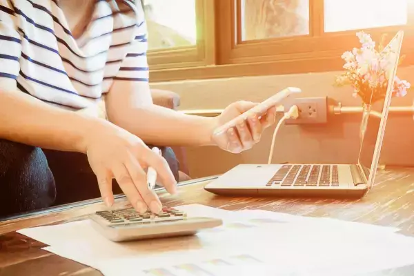 mulher comparando informações com calculadora, celular e notebook