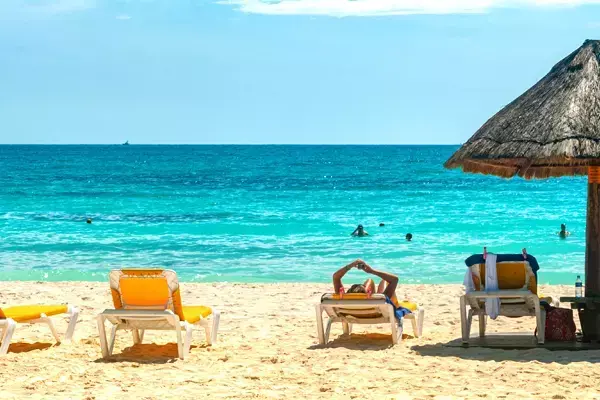 Foto mostrando uma pessoa deitada em uma cadeira de praia enquanto outras tomam banho no mar, em uma das praias de Cancún, no México.