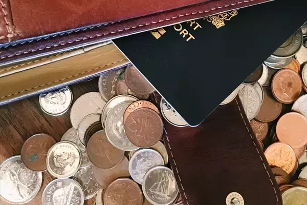 Imagem mostrando moedas sobre uma mesa, com um passaporte em cima delas.