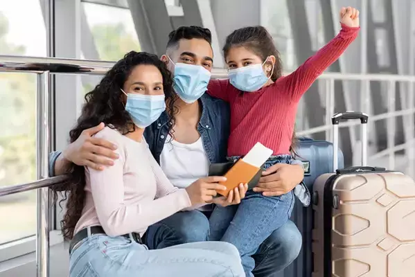 Um homem, uma mulher e uma criança abraçados ao lado de uma mala. Todos prontos para embarcar.