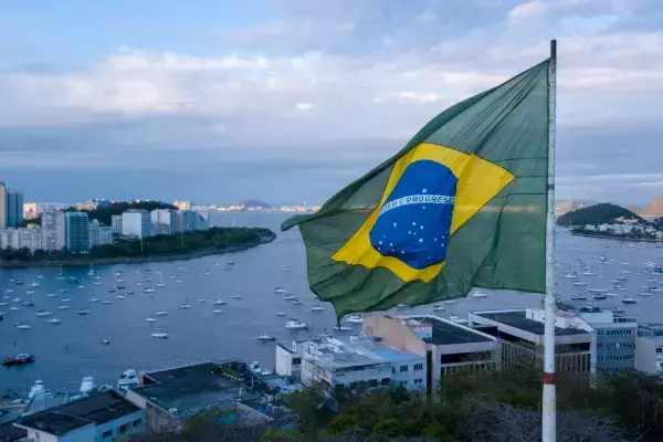 Bandeira do Brasil hasteada com paisagem de mar e construções urbanas ao fundo