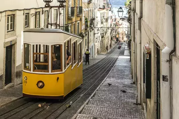 Foto de um pequeno trem amarelo cercado pelos prédios das ruas de Portugal.