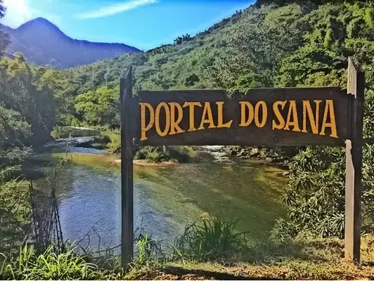 Uma entrada de madeira escrito portal do Sana, em frente a uma cachoeira.