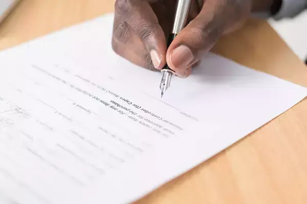 Imagem da mão de uma pessoa assinando um contrato.