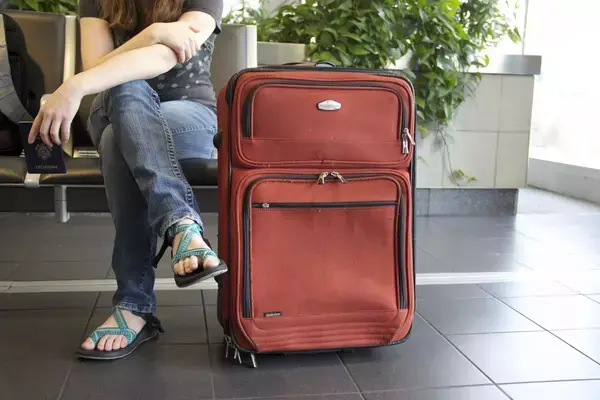 Uma passageira sentada no aeroporto ao lado de uma mala.