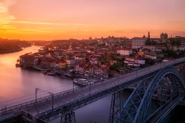 Foto mostrando o pôr do sol de Porto, com destaque para a Ponte D. Luís e vários edifícios ao fundo.