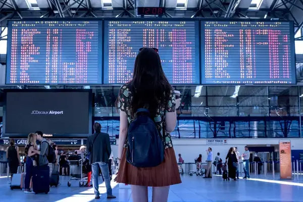 Foto das costas de uma mulher encarando a janela de um aeroporto a noite.