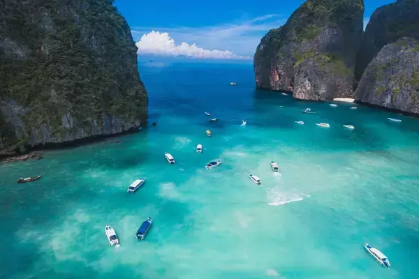 Foto das águas da Ilha de Phuket, na Tailândia, mostrando as rochas e alguns barcos entre elas.