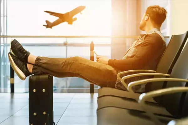 Foto de uma pessoa sentada no aeroporto esperando o seu voo, enquanto observa um avião pela janela.