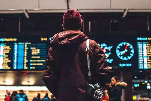 Foto de uma pessoa para em frente ao painel de voos de um aeroporto.