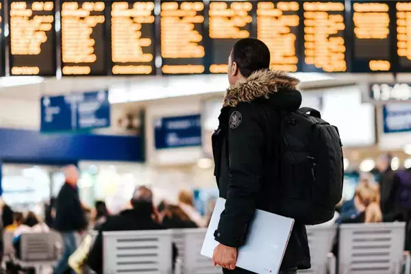 Foto de uma pessoa dentro de um aeroporto observando o painel dos voos.
