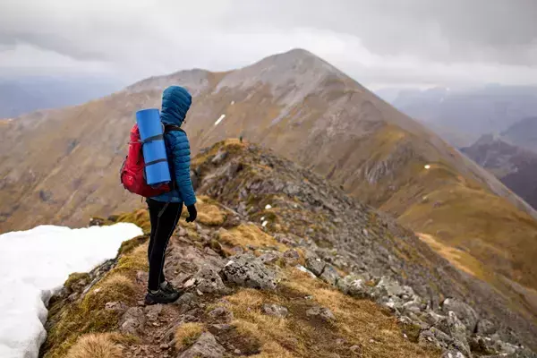 Foto de uma pessoa no pico de uma montanha observando a paisagem.