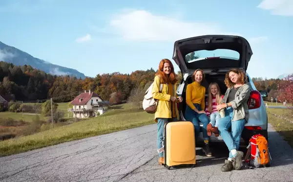 Foto de uma família prestes a viajar. Ao todo, são 4 mulheres sentadas em um porta malas aberto, com bagagens rodeando elas.