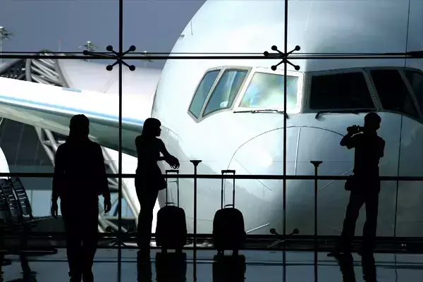 Foto de três pessoas no aeroporto, em frente a uma janela com a vista para um avião.
