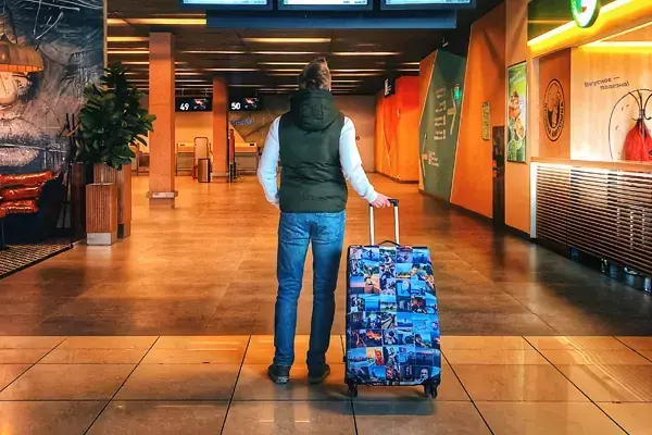 Pessoa para dentro de um aeroporto vazio, olhando pra frente enquanto segura uma mala.