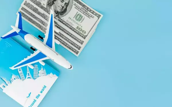 Um avião em cima de uma mesa azul, ele está posicionado ao lado de algumas notas de dólares e um passaporte.