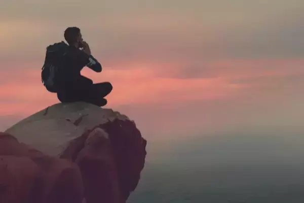 homem do alto de pedra observando o por do sol