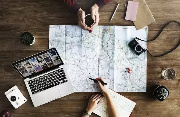 casal analisando mapa, com câmera, notebook e outros itens que remetem a viagem
