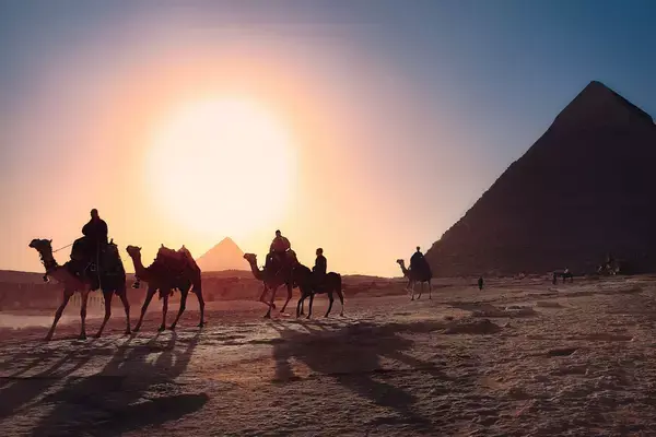 Pessoas em camelos em frente as pirâmides egípcias