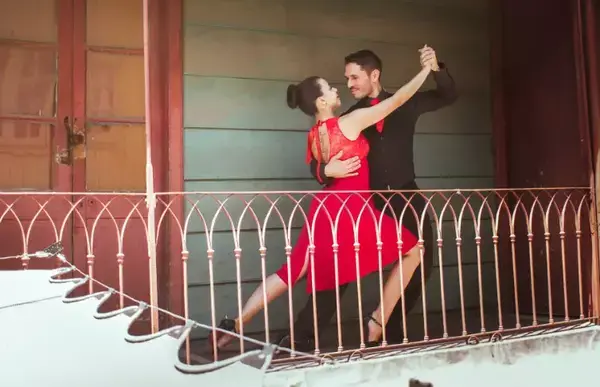 Uma mulher e um homem dançando tango perto de uma grade.
