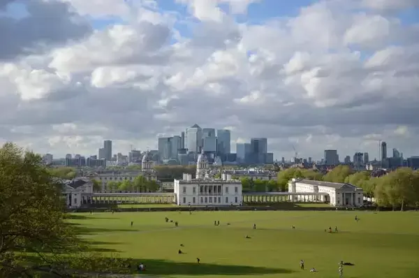 Pessoas andando na grama do Greenwich Park, e edifícios de Londres aparecendo ao fundo