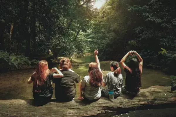 Quatro amigas na natureza, em local com riacho e árvores