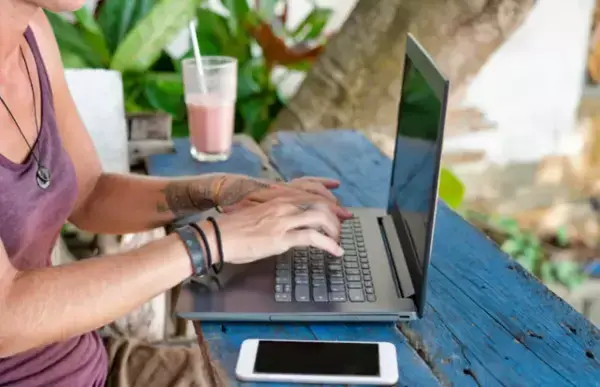 Um moço mexendo no computador em uma espécie de praia, fora do escritório.