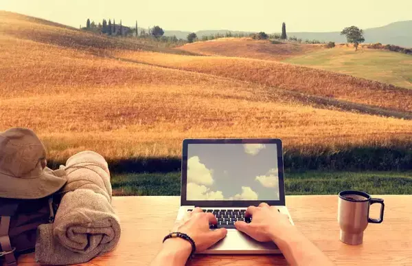 Um homem mexendo no computador em uma espécie de campo rural.