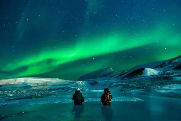 Viajantes na neve durante a noite olhando a aurora boreal
