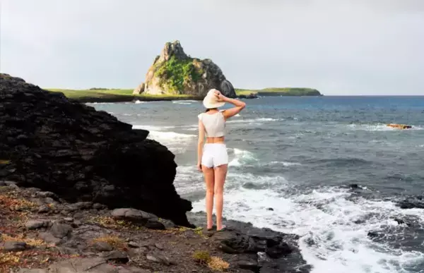 Uma mulher em cima de umas rochas olhando para o mar.
