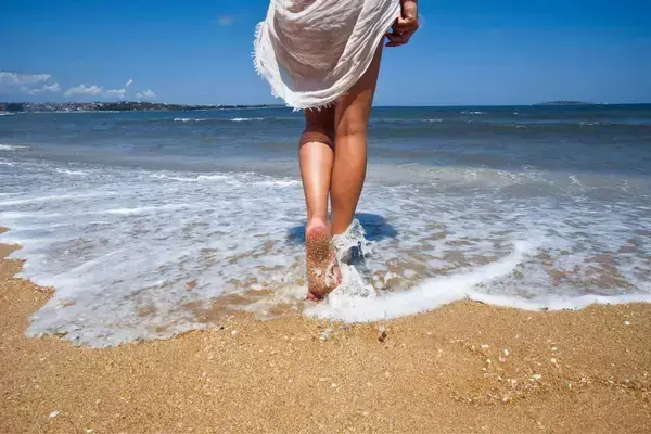 Mulher na areia de praia entrando no mar