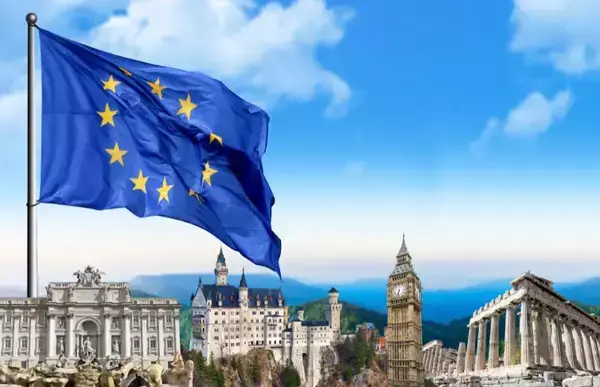 A bandeira azul da União Europeia em primeiro plano, em segundo uma cidade ao luz do dia.