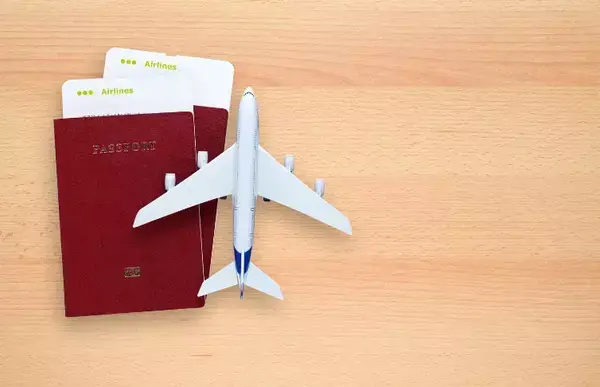 Um passaporte vermelho em cima de uma mesa, sob ele um avião branco em miniatura.