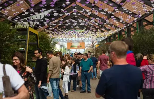 Um stand em uma espécie de feira, como diversas pessoas e modelos de plantas.