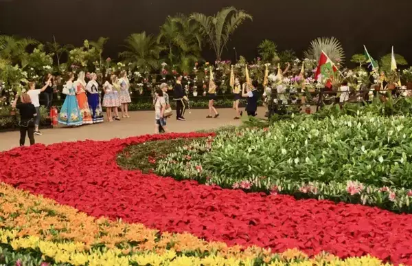 Um parque lotado de flores com alguns turistas passando por perto.