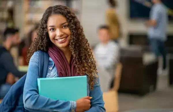 Uma menina segurando um caderno e sorrindo para a câmera.